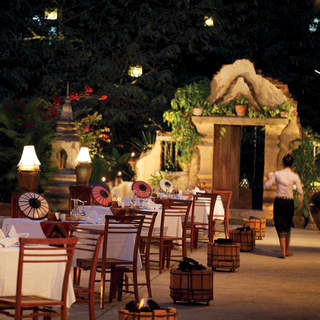 Row of outdoor restaurant tables in evening light surrounded by gardens