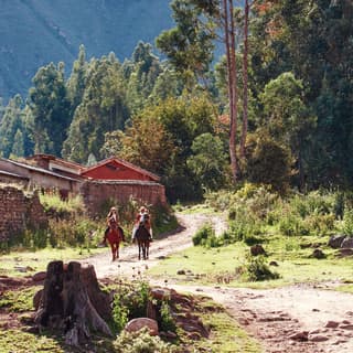 Two horseback riders trotting along a path in Sacred Valley