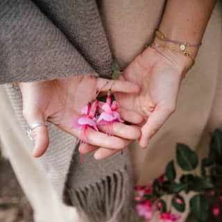 A young woman delicately holds pink fuchsia flowers in her hands