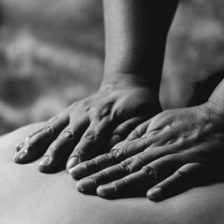 Black and white close-up of hands pressing on to the back of a guest experiencing a Mayu Willka massage at the spa.