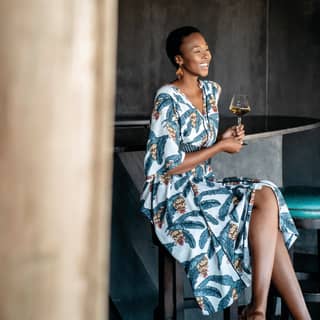 Lady in a tropical print dress smiling and holding a glass of wine in an open-sided bar