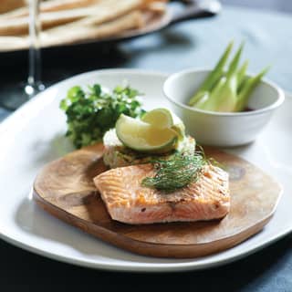 Close-up of smoked salmon and a fish cake on a wooden platter garnished with lime