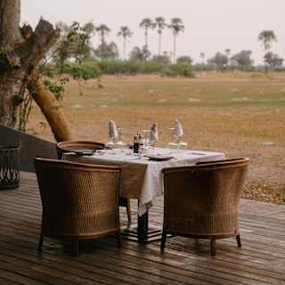 A dining table with three wicker tub chairs awaits guests at the edge of the restaurant deck overlooking the plains.