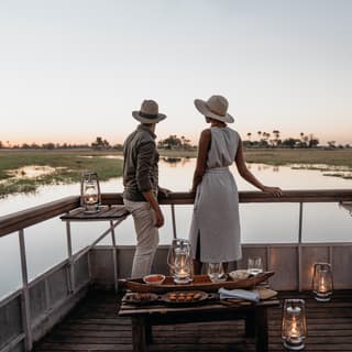 A couple standing on the bow of a candlelit boat at sunset in the Okavango Delta