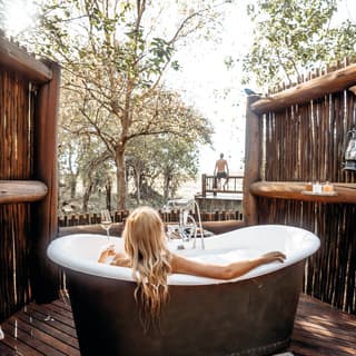 Lady with long blonde hair relaxing in a copper rolltop bath outside