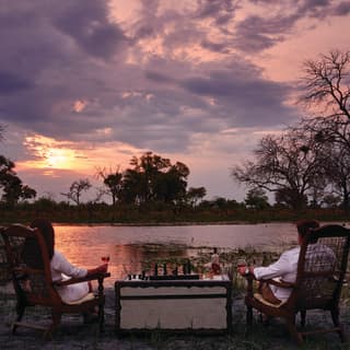 A couple at a private dining table overlooking a safari watering hole at sunset