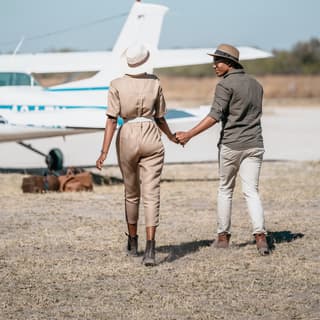 A couple holding hands and strolling along a runway towards a small aircraft