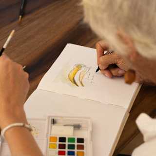 Vicki Thomas writes a message beneath a watercolour-filled sketch of a yellow-billed hornbill bird in a white art pad.