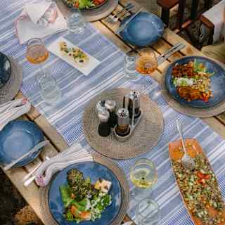 Looking down on a bush lunch for four with rosé and white wine, and blue dinner plates filled with vibrant fresh salads.