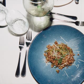 An African dish of meat and grains sings of umami on a blue dish, seen from above on a table with cutlery, water and wine.