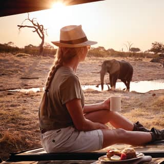 A guest enjoys her breakfast watching an elephant at the water hole nearby