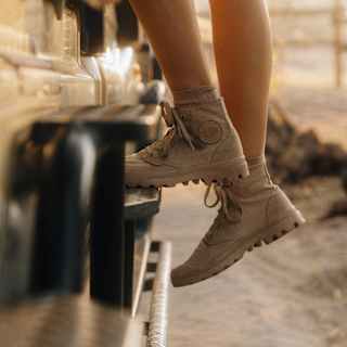 A woman with bare legs, wearing beige safari shoes, mounts a game viewing jeep in a close-up taken from the knees down.