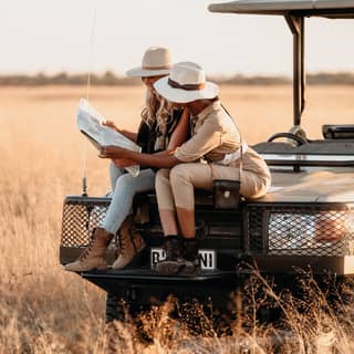 Two guests check a map while sitting on the front of the Belmond safari vehicle while out in the bush