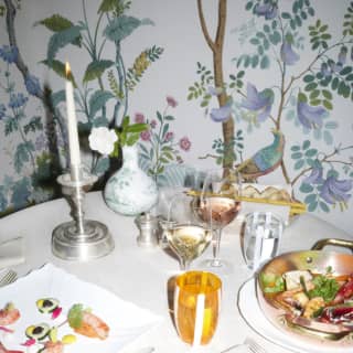 A table is set for two in a private corner decorated with colourful botanical painted walls. The plates are artworks of seafood