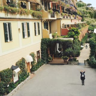 The concierge waves from the hotel's courtyard, surrounded by lush wall-hugging ivy and a long hedge of pink roses