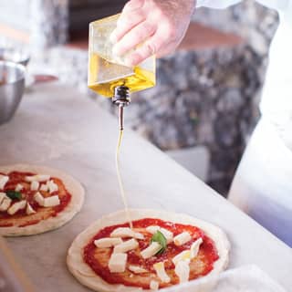 Olive oil being drizzled over freshly made pizza dough topped with tomato puree