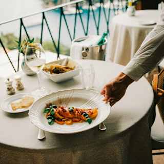 A waited sets down a plate of richly sauced spaghett'oro with tomatoes in three textures at a sea-view table at La Terrazza.