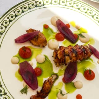 Grilled lobster tail and claws, served with red onion and a green, herby oil on a white plate with a green patterned rim.