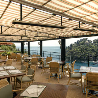 A striped awning throws shade across the restaurant balcony, each table graced with stunning views of Portofino Harbour