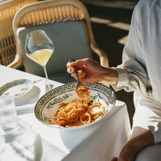 Sunlight falls on a dining table where a guest enjoys spaghetti with rich tomato sauce with a drink at Splendido Grill.
