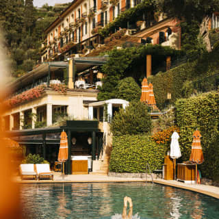A swimmer performs an underwater handstand in the cobalt pool, with a hotel backdrop of saturated terracotta and cream.