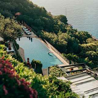Action shot as a guest is captured mid-air diving into the glass-like pool, in a view from above over gardens and sea.