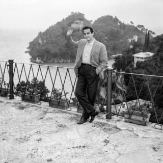 A 1950s image of Marlon Brando leaning against the balcony railings and waving. Behind him the hill plunges to the sea