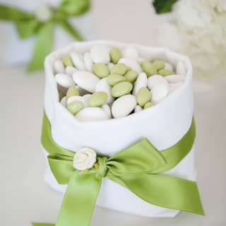 Wedding favours of green and white sugared almonds fill small white sacks tied with pale green ribbons and cream silk flowers