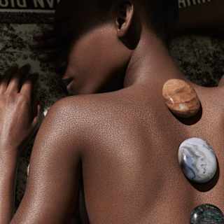 Three glossy pebbles of different hues lie vertically along the spine of naked back, seen in a close-up spa detail.