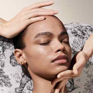 A therapist's hands cup the forehead and chin of a female spa guest during a facial treatment, seen in a Spa Dior detail.