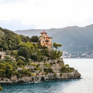 The peach pastel Villa Beatrice, with a turret, rises from trees and terraced garden on the rocky headland of Baia Canone.