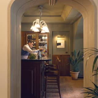 Sideview of the bar and three stools, the barman prepares a drink