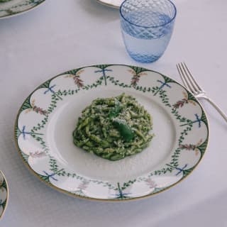 Close up of a pesto pasta dish on an ornate porcelain plate with a garland pattern