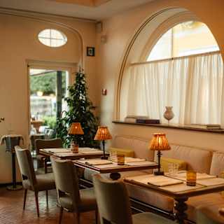 Looking at a row of tables for two, with glowing lamps, wall banquettes and dining chairs in the mellow interior of Dav Mare.