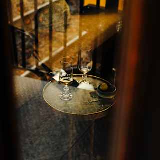 Two tasting glasses, each with a nip of whisky, rest on a round side table, viewed through a glass-panelled window.
