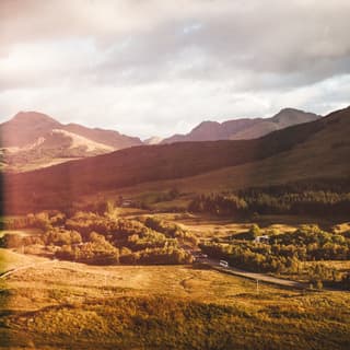 In honey light, a road cuts through the landscape as distant hills and peaks weave a Highland tapestry of shapes and shadows.