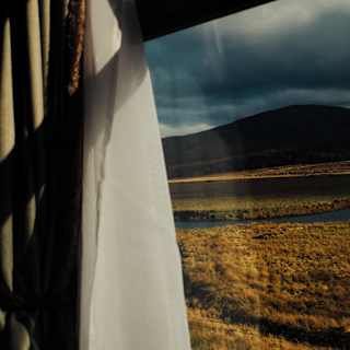 Heavy-bottomed clouds hang over a dark mountain in a view through a train window across bronze grassy plains.