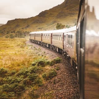 Exterior of gleaming burgundy train carriages curving through a Scottish valley