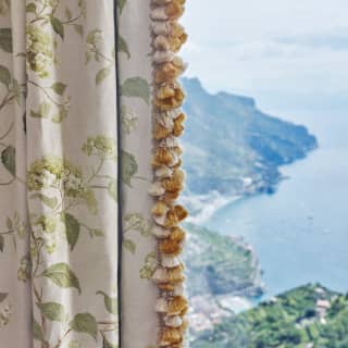 Behind a half-closed curtain, a window reveals extensive views of the bays and contours of the incredible Amalfi Coast.