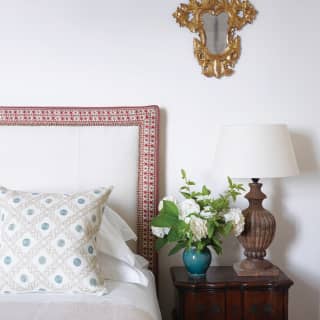 A detail of the Miramare suite bed shows bright linen, a headrest with red embroidery piping and table with fresh flowers.