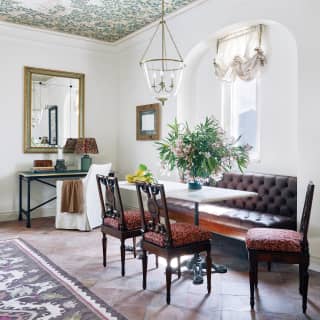 The marble-top dining table with chairs and bench seating is flooded with natural light from the adjacent window.