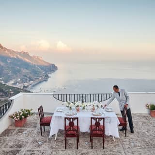 A staff member lays the dining table on Villa Margherita's rooftop terrace for a sublime sunset meal overlooking the coast.