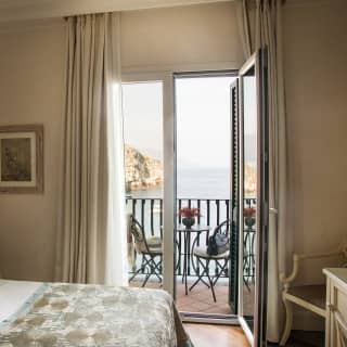 An elegant bedroom of soft creams and sage enjoys a private balcony with unrivalled views across the Bay of Mazzarò
