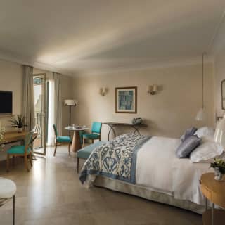 Open doors offer unrivalled views of the sea. A king bed is topped with grey satin pillows and flanked by hanging lamps