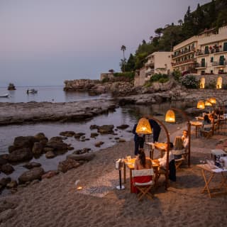 Diners are served on a private beach, their tables illuminated under private pools of light from tulip-shaped lamp stands