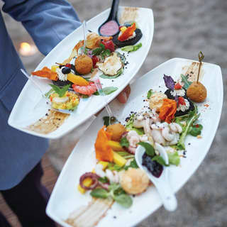 A waiter carries two large white plates in one hand, filled with brightly coloured salad leaves, arancini balls and seafood