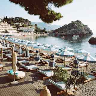 Rows of blue and white parasols and loungers follow the sweep of Mazzarò Bay in a beautiful image of Lido Villeggiatura.