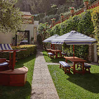 A path divides the Kids Club garden lawn, with a pirate ship frame to the left, and two parasol-shaded tables on the right.