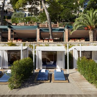 Row of luxurious beach cabanas lining a shore with blue sunbeds in front