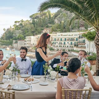 Guests at a formal wedding table on an outdoor terrace overlooking Taormina